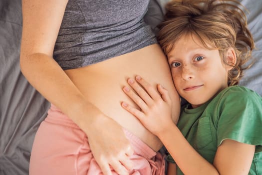 Young beautiful pregnant woman and eldest son. The cute boy leaned his ear against his mother's belly. Expecting a baby in the family concept. Preparing an older child for a younger one.