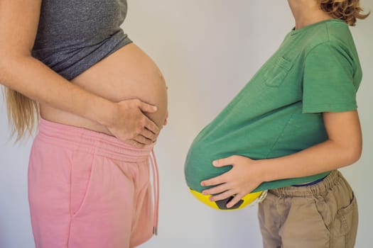 Amusing son. Pregnant beautiful woman amusing her little son while putting yellow ball under his green shirt.