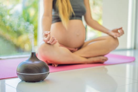 Young pregnant woman doing yoga exercises and meditating at home with an aroma diffuser. Health care, mindfulness, relaxation and wellness concept. Aromatherapy during pregnancy.