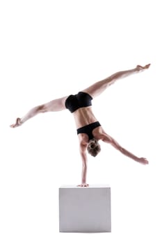 Slim acrobat balancing on cube in studio, isolated over white background