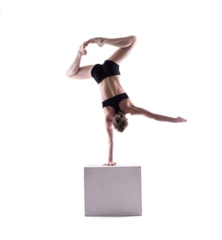 Graceful acrobat posing on cube in studio