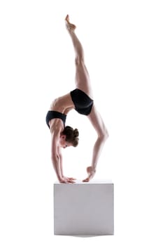 Pretty gymnast posing on cube in studio, isolated over white background