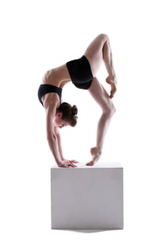 Attractive young woman posing on cube in studio, isolated over white background