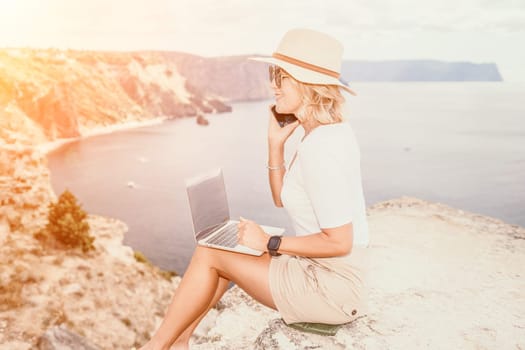 Digital nomad, Business woman working on laptop by the sea. Pretty lady typing on computer by the sea at sunset, makes a business transaction online from a distance. Freelance remote work on vacation