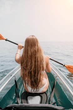 Woman in kayak back view. Happy young woman with long hair floating in transparent kayak on the crystal clear sea. Summer holiday vacation and cheerful female people having fun on the boat.