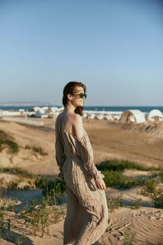 an elegant woman in a beige dress walks on the sand against the backdrop of the sea visible in the distance. High quality photo
