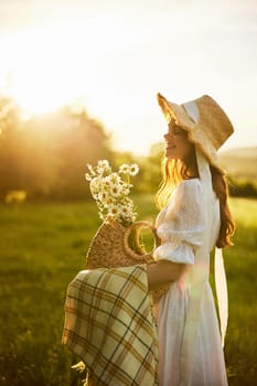 portrait of a beautiful, happy girl in a light dress, a wicker hat and with a basket of daisies posing against the backdrop of the setting sun in the field. High quality photo