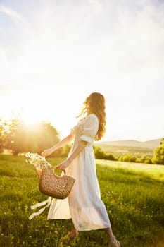 a woman in a light dress in a chamomile field against the background of a sunset stands with her back to the camera with a basket of flowers in her hands. High quality photo