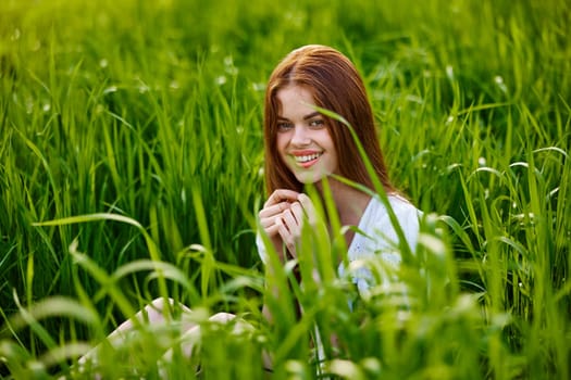 portrait of a beautiful, happy woman sitting in the grass in a light dress and smiling at the camera. High quality photo