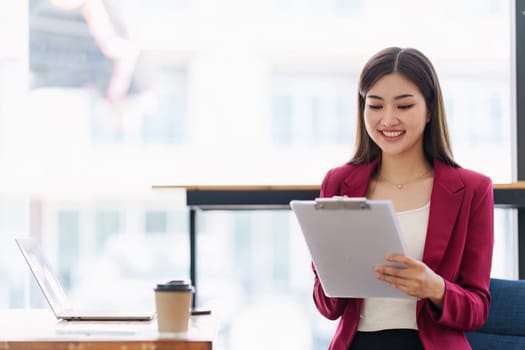 Smiling Asian Banker makes financial report and studies annual figures, analyzes profits. Accountant checks status of financial.