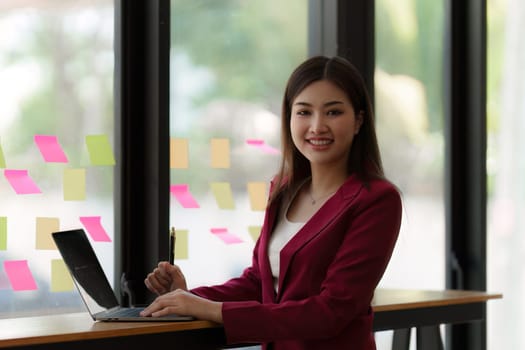 Smiling Asian Banker makes financial report and studies annual figures, analyzes profits. Accountant checks status of financial.