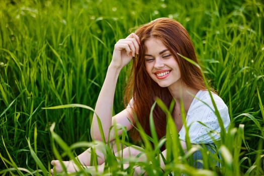 portrait of a beautiful, happy woman sitting in the grass in a light dress and smiling at the camera. High quality photo