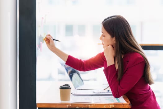 Smiling Asian Banker makes financial report and studies annual figures, analyzes profits. Accountant checks status of financial.