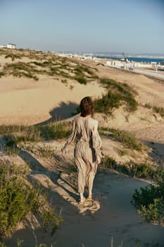 a woman walks on the sand away from the sea in windy weather enjoying the pleasant weather with her back to the camera. High quality photo