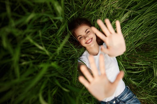 laughing redhead woman stretching her palms to the camera while lying on the grass. High quality photo