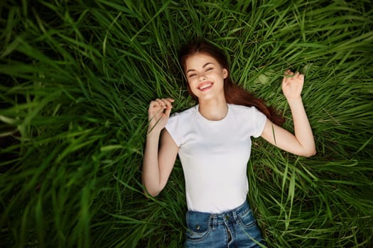 a woman with even, white teeth laughs in the green grass. High quality photo