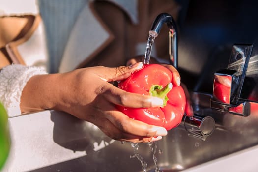 close up of the hands of a woman washing a red pepper in the sink of a camper van, concept of fresh local product and healthy cooking in nomadic lifestyle