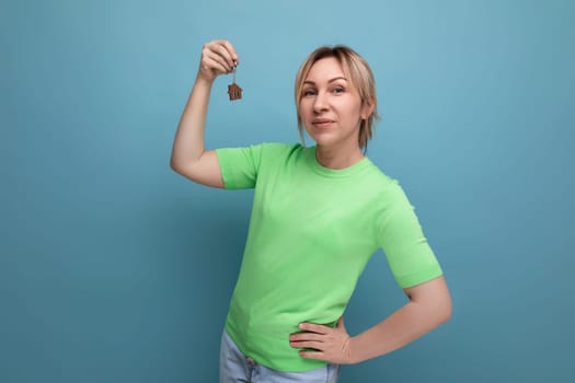 close-up of lucky cute blond woman in casual look holding apartment keychain on blue background.