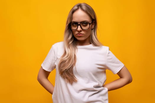 girl student in glasses and a white T-shirt on a studio yellow background.