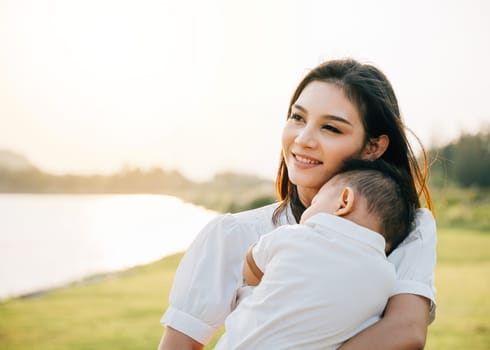 A heartwarming Mother's Day moment captured in the park at sunset. Beautiful mother cradles her sleeping baby, basking in peaceful nature and lovingly smiling at her newborn. Family care at its finest