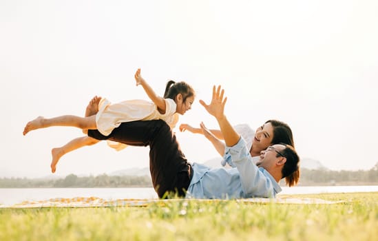 Family fun. Happy family father holding small kid daughter on straight legs with mother in the park, child girl smiling flying in air play airplane, little girl open arms and flying like plane