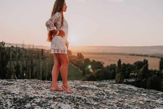 Romantic beautiful bride in white dress posing with sea and mountains in background. Stylish bride standing back on beautiful landscape of sea and mountains on sunset