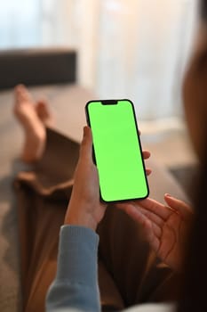 Close up view of woman using smart phone, relaxing on couch at home. Green screen for your advertising text message.