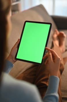 Close up view of casual young woman using digital tablet on couch at home. Green screen for montage your graphic display.