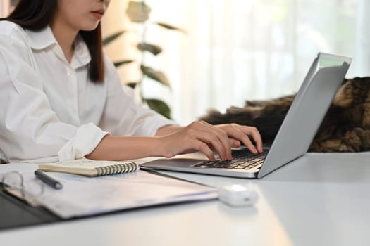 Cropped shot of young woman typing business email, working online on laptop at home office.