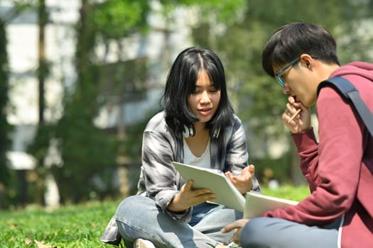 Two university student reading books, preparing for exam while under tree at sunny beautiful day. Education and lifestyle concept.