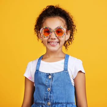 Girl child, happy and sunglasses in studio portrait with smile, summer style and yellow background. Mixed race model, female kid and fashion frame on face with kids clothes, aesthetic and lifestyle.