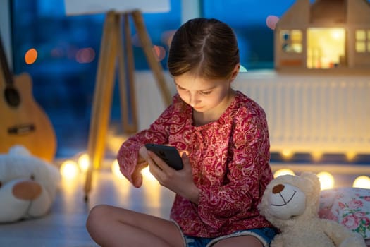 Cute little girl using phone at night sitting on floor in playroom