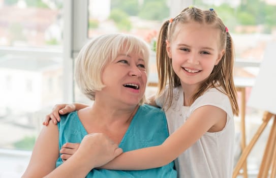 Portrait of happy grandmother hugging with little granddaughter indoors