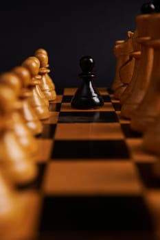 Selective focus on a black pawn between white chess pieces on the chessboard, isolated on black background. The concept of competition, battle, development of leadership, business strategy and risks