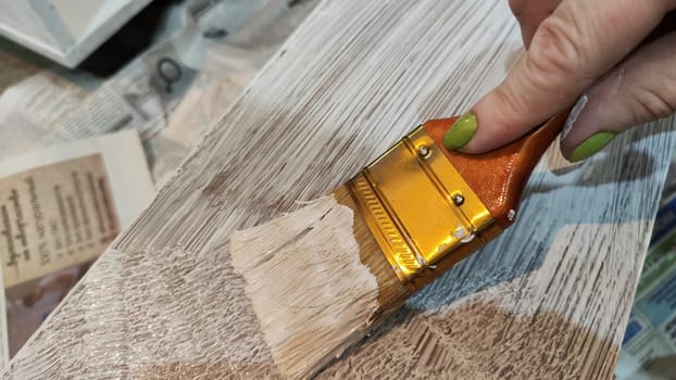 Woman hand painting on wooden boards with Brush full of white paint. Painting of new wood board or furniture and old newspaper on background. Partial focus