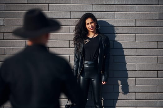 Beautiful couple in black clothes together against wall outdoors.