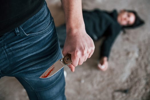 Murderer with knife covered in blood standing near his dead female young victim.