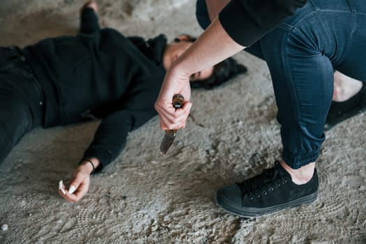 Murderer holding knife that covered in blood and sitting near his dead female young victim.