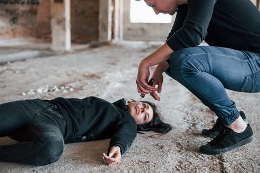 Murderer holding knife that covered in blood and sitting near his dead female young victim.