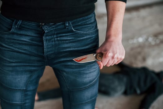 Murderer with knife covered in blood standing near his dead female young victim.