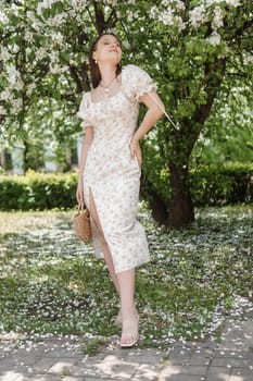 An attractive long-haired woman walks in the spring in the park of blooming apple trees. Spring portrait of a woman