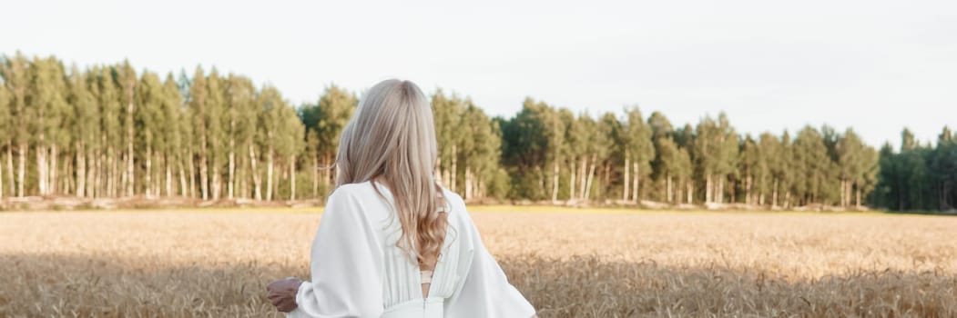 A blonde woman in a long white dress walks in a wheat field. The concept of a wedding and walking in nature