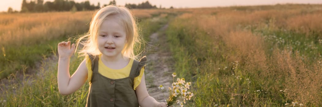 A little blonde girl is sitting walking on a chamomile field and collecting a bouquet of flowers. The concept of walking in nature, freedom and a clean lifestyle