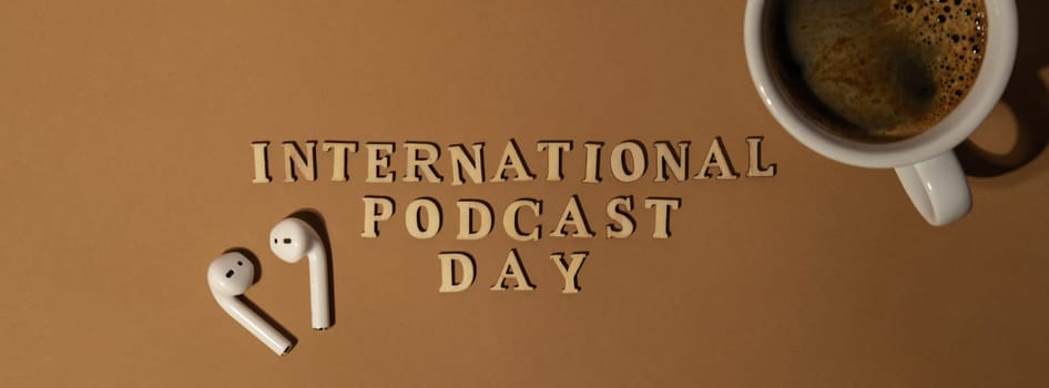 Announcement text INTERNATIONAL PODCAST DAY on beige background with white cup of coffee wireless headphones. Podcasting concept. Listening radio audio healing wellness sound health habits