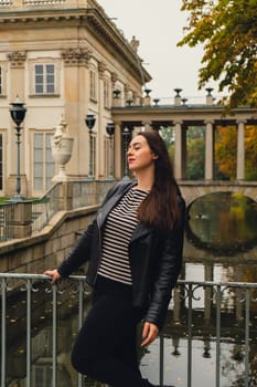 Tourist attraction woman travel enjoying nature sightseeing Baths classicist Palace on the Isle in Lazienki Park touristic place in Warsaw. Lazienki Royal Baths Park, Warsaw Poland. Colorful Autumn Foliage and Mirror Reflection on the Lake. Yellow leaves Nature in autumn Baroque columns