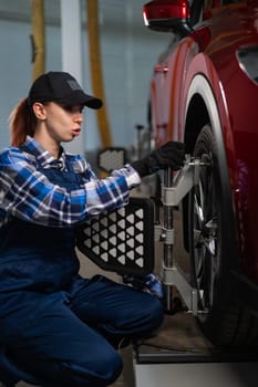 A female auto mechanic makes a camber. Woman working in a car service