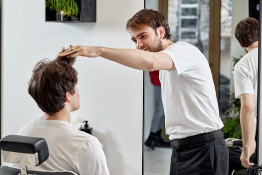 Barber talking to caucasian man while sitting in chair before haircut at barbershop