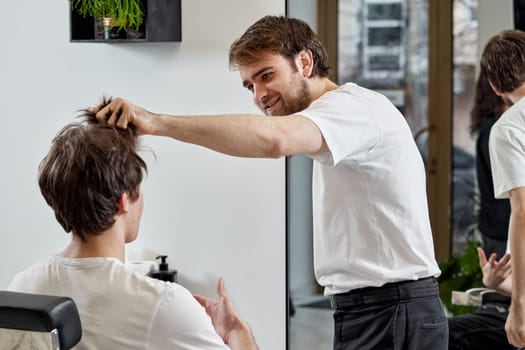 friendly barber talking to caucasian man while sitting in chair before haircut at barbershop. client tells what haircut he wants