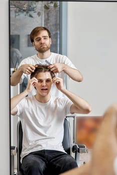 Barber talking to caucasian man while sitting in chair before haircut at barbershop. client tells what haircut he wants