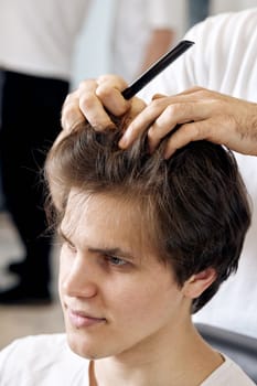 professional male hairstylist combing young customer's hair in barbershop